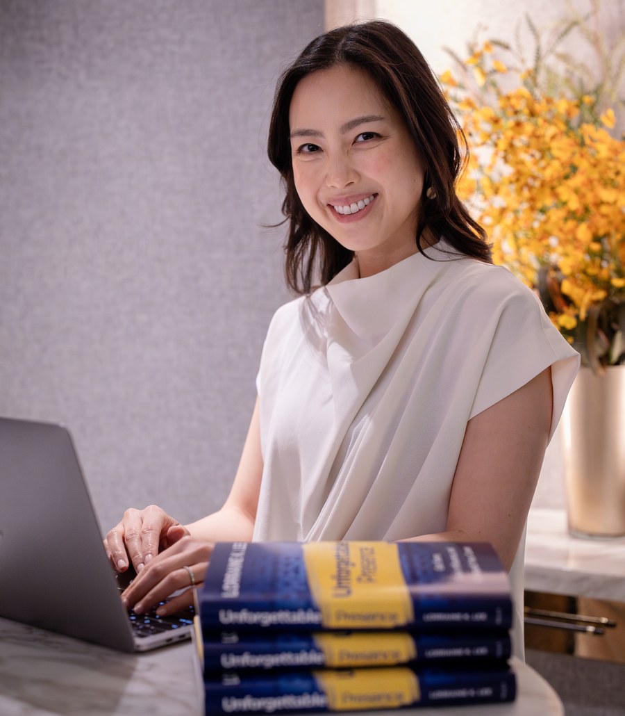 Lorraine K. Lee at her laptop beside a stack of her book Unforgettable Presence